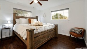 Een slaapkamer met een houten bed, een plafondventilator, een nachtkastje, een stoel en een raam met uitzicht op bomen.