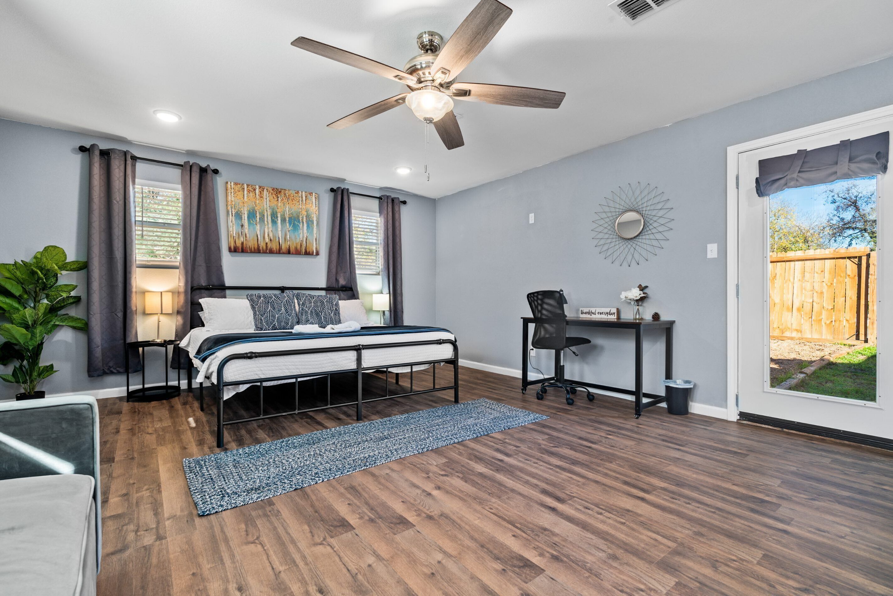 Une chambre à coucher comprenant un lit, un bureau, une chaise, un ventilateur de plafond et une vue sur l’extérieur.