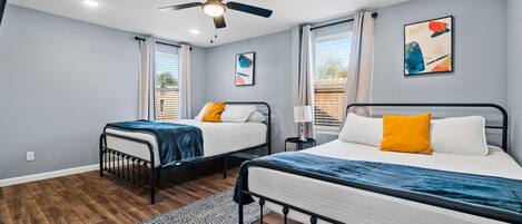 A bedroom with two beds, a ceiling fan, and artwork on the walls.