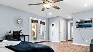 Une chambre à coucher comprenant un lit, un ventilateur de plafond, un bureau avec une chaise et un téléviseur fixé au mur.