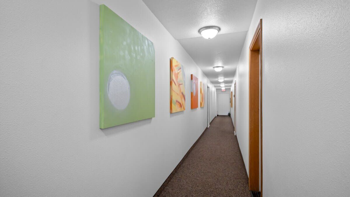 Un couloir aux murs blancs, doté d’un tapis marron et orné de plusieurs œuvres d’art encadrées.