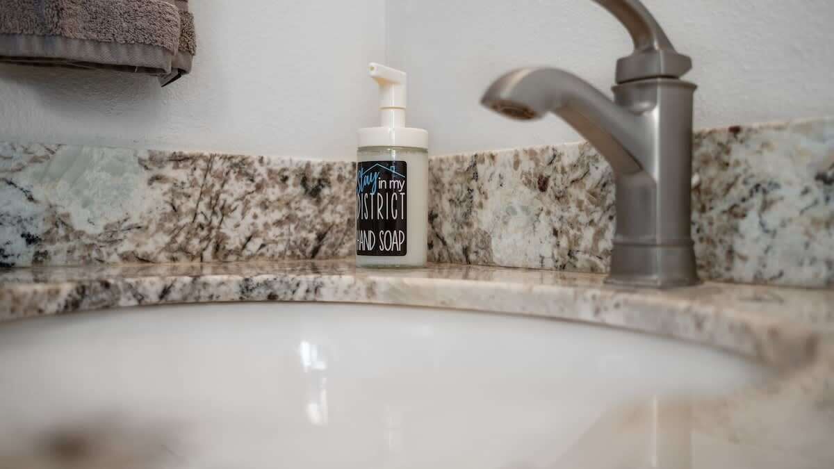 A bathroom sink with a marble countertop, a hand soap dispenser, and a faucet.