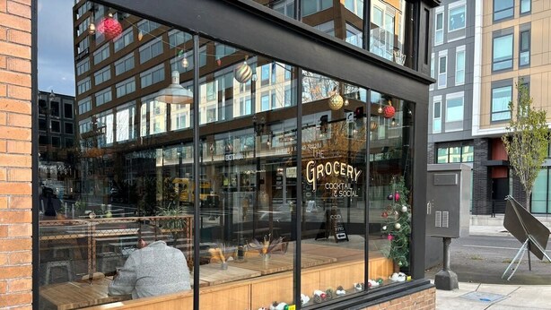 A storefront with a large window displaying a Christmas tree and ornaments. The sign reads "The Grocery Cocktail & Social." - #StayInMyDistrict Downtown Loft2 (Vancouver)