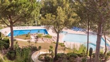 A pool area with a curved pathway, surrounded by trees and a clear blue pool.