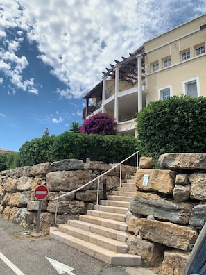 Una scala in pietra conduce a un edificio con un balcone, un segnale di divieto di accesso e un cartello che indica che l'immobile è in vendita.