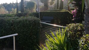 Un chemin de jardin agrémenté d’un portail en métal, entouré de différentes plantes et d’arbres.