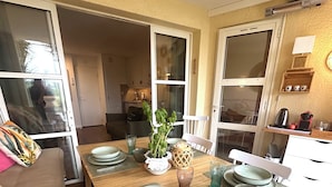 Een eetgedeelte met een houten tafel gedekt voor vier personen, omringd door een bank en een keuken op de achtergrond.