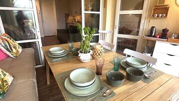 Un coin repas avec une table en bois dressée pour quatre personnes, entourée d’un canapé et avec une cuisine en arrière-plan.