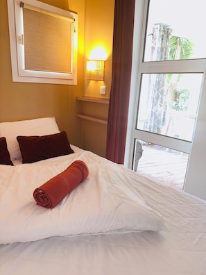 Una camera d'albergo con un letto, una lampada da comodino, una finestra con tende e vista esterna.
