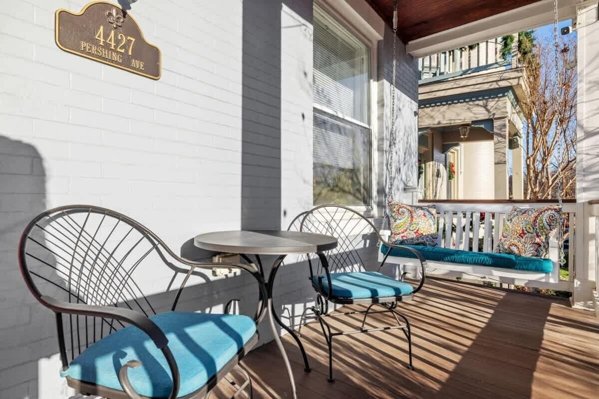 Une véranda avec une clôture blanche, un banc bleu avec coussin et une table et des chaises en métal.