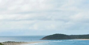 A coastal landscape with a beach, ocean, and a hill in the distance.