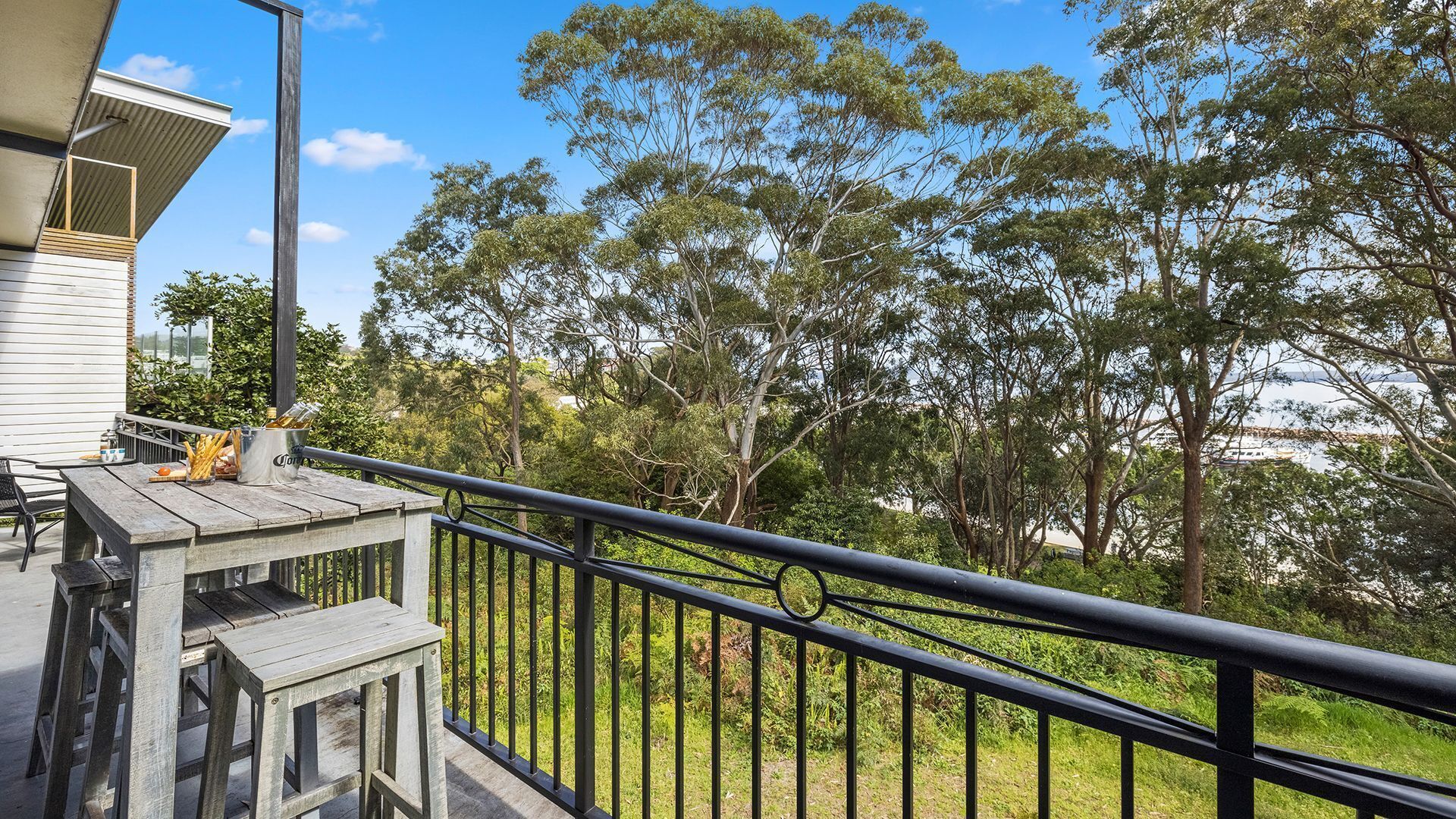 A balcony with a wooden table and chairs, a metal railing, and a view of trees and a body of water.
