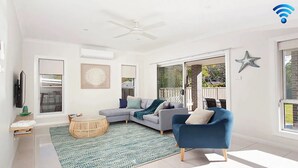 A modern living room with a grey sofa, a blue armchair, a round coffee table, and a starfish decoration on the wall. - CALM at Shoal Bay - Gorgeous brand new, modern home (Shoal Bay)