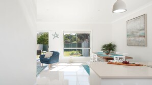 A bright, modern kitchen with a large island, white cabinetry, and a view of the backyard through a sliding door. - CALM at Shoal Bay - Gorgeous brand new, modern home (Shoal Bay)