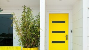 Un bâtiment avec une porte jaune vif et un grand plant de bambou devant.
