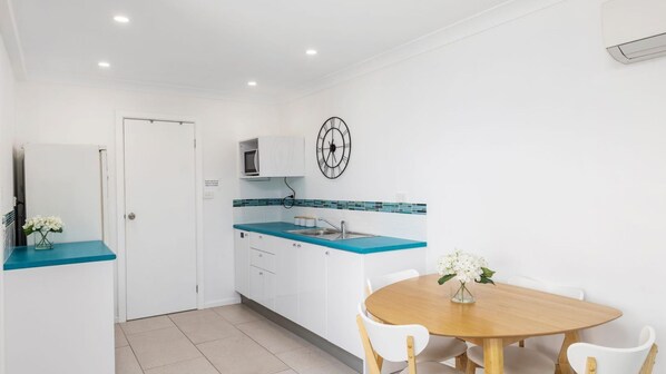 A compact kitchen with white cabinets, a blue countertop, and a wall-mounted clock. - Embracing Dutchies – ocean and beach views (Nelson Bay)