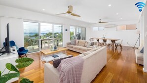 Un salon moderne avec un canapé, une table basse et un coin repas avec des chaises. Une grande fenêtre offre une vue sur l’extérieur.