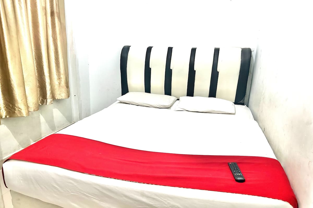 Una cama con una colcha blanca y roja, dos almohadas y un control remoto sobre la misma.
