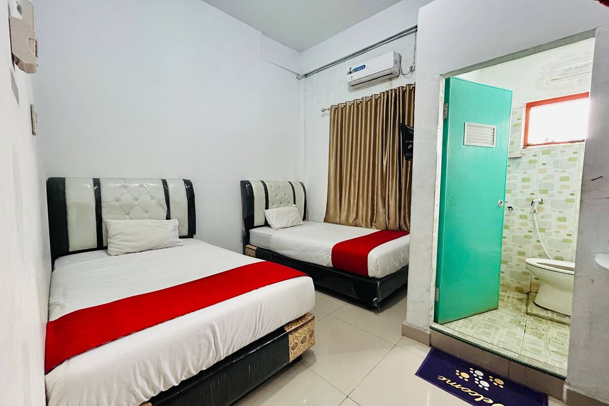 Habitación de hotel con dos camas, baño y ventana con cortinas.