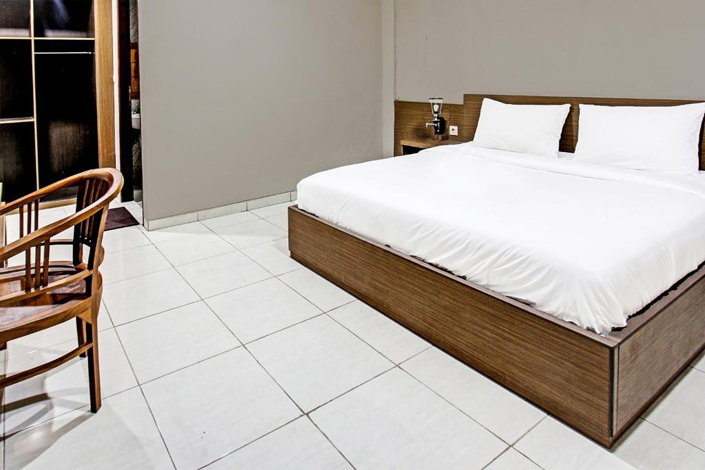 Una cama bien hecha con ropa blanca en una habitación con piso de baldosas blancas y un cabecero de madera.