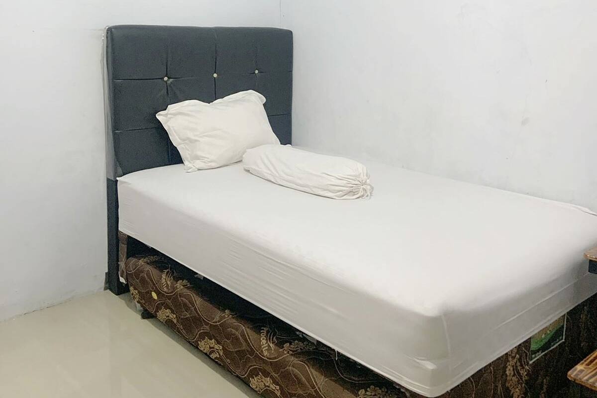 Una cama individual con cabecera oscura, ropa de cama blanca y un tapete estampado al pie de la cama.