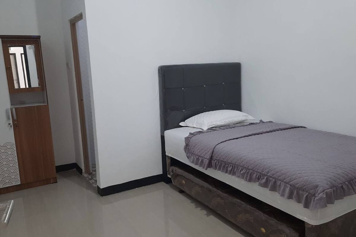 Una cama individual con cabecera oscura, almohada blanca y manta púrpura.
