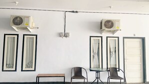Quarto com dois aparelhos de ar condicionado fixados na parede, um banco, duas cadeiras e uma porta.