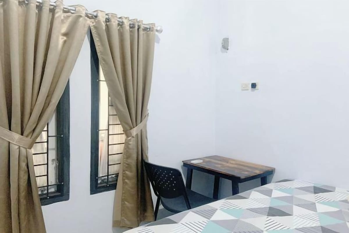 A room with a bed, a small table, and two windows with curtains.