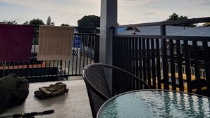Uma área externa coberta com mesa e cadeiras de vidro, guarda-corpo de metal e vista do céu.