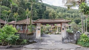 A traditional building with a tiled roof, surrounded by lush greenery and a stone wall. - Baruna Lakeside View (Kintamani)