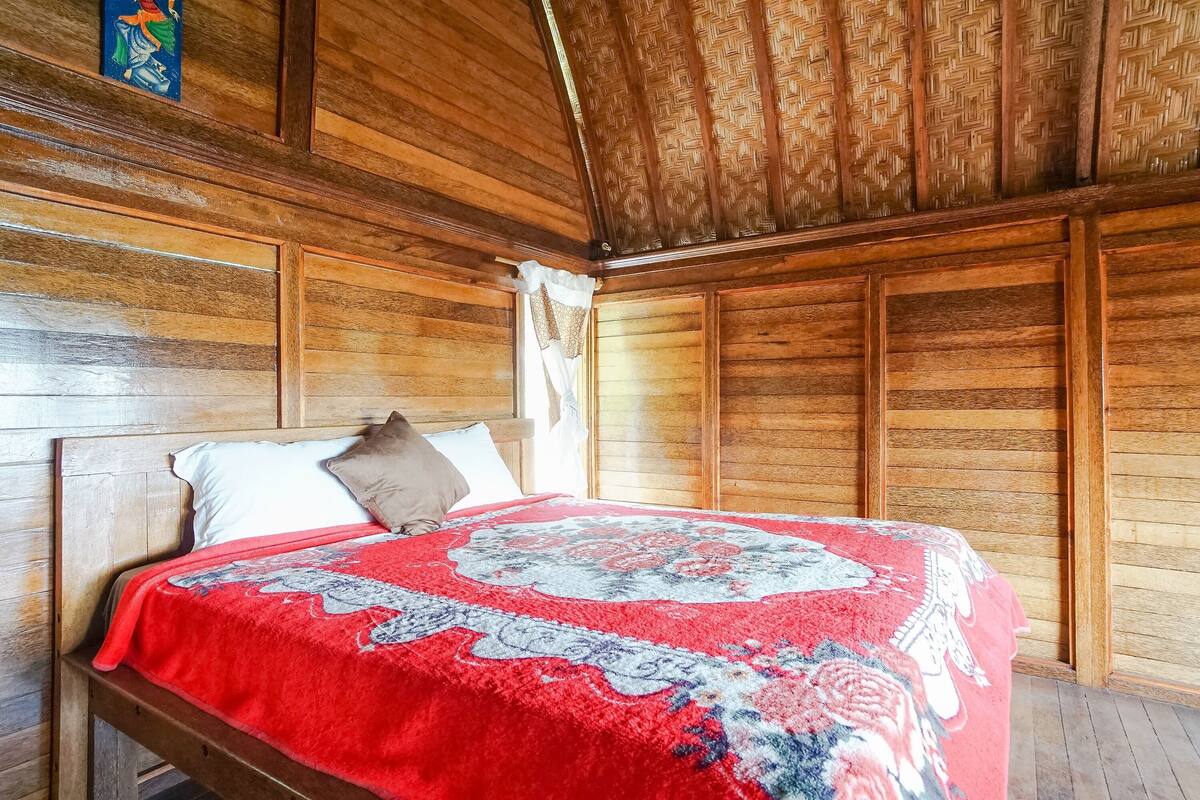 Habitació de fusta amb un llit, sostre de fusta i un disseny de sostre trenat.