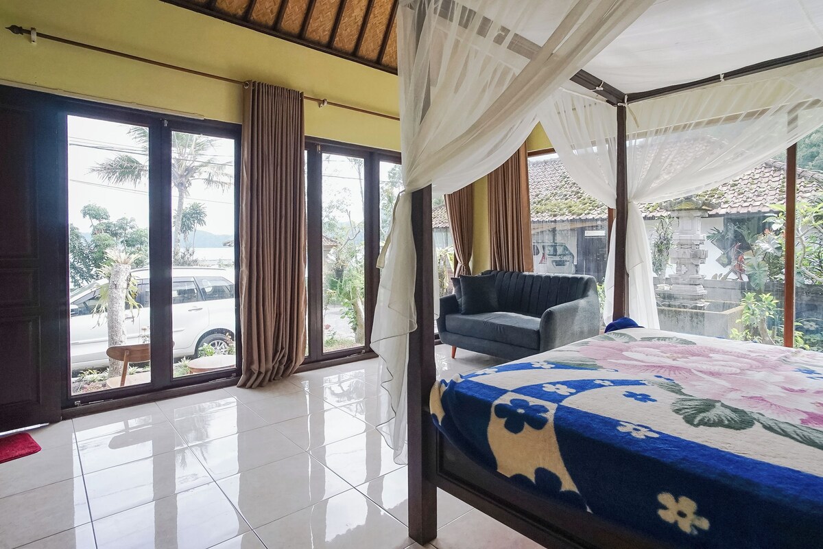 A room with a bed, a chair, and large windows with curtains.