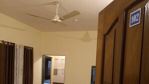 A hallway with a ceiling fan, a door labeled "102", a refrigerator, and a chair. - Springfield Family Apartment (Mahabaleshwar)