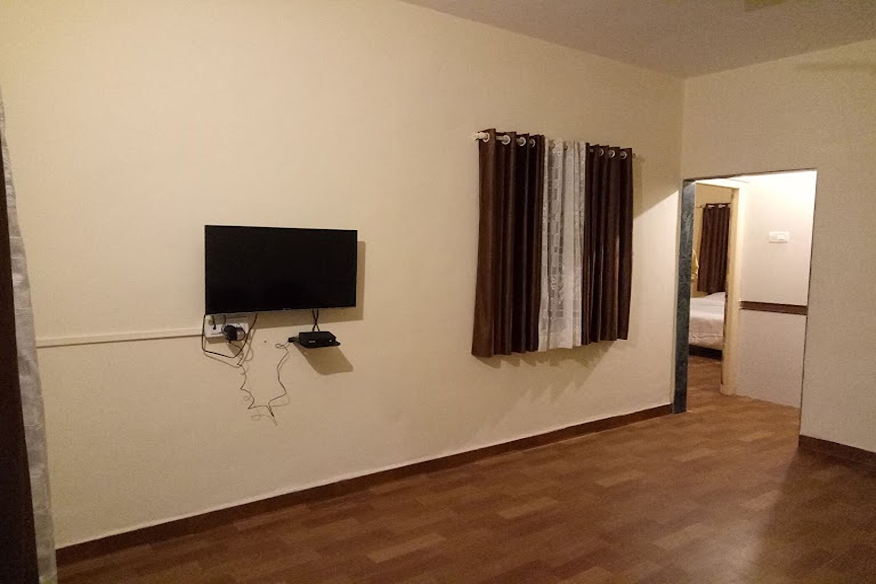 A room with a flat-screen TV mounted on the wall, a wooden floor, and a door leading to another room.