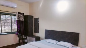 A hotel room with a bed, a desk, a chair, and a window with curtains. - Springfield Family Apartment (Mahabaleshwar)