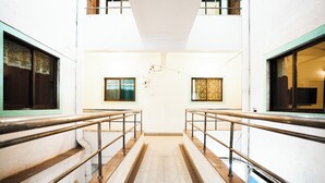 A corridor with a central staircase, metal railings, and patterned windows. - Springfield Family Apartment (Mahabaleshwar)