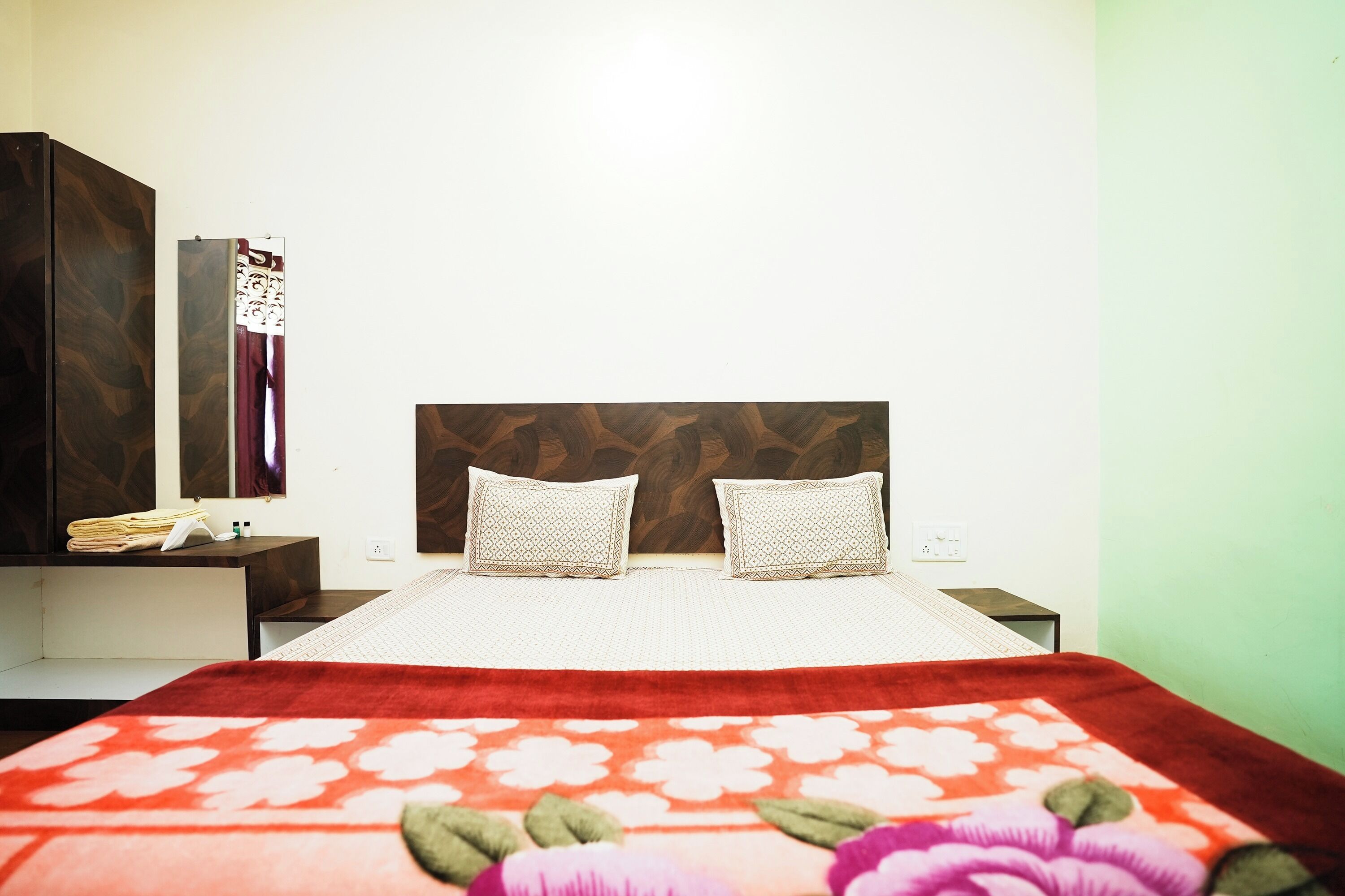 A neatly made bed with a red floral blanket, two pillows, and a wooden headboard.