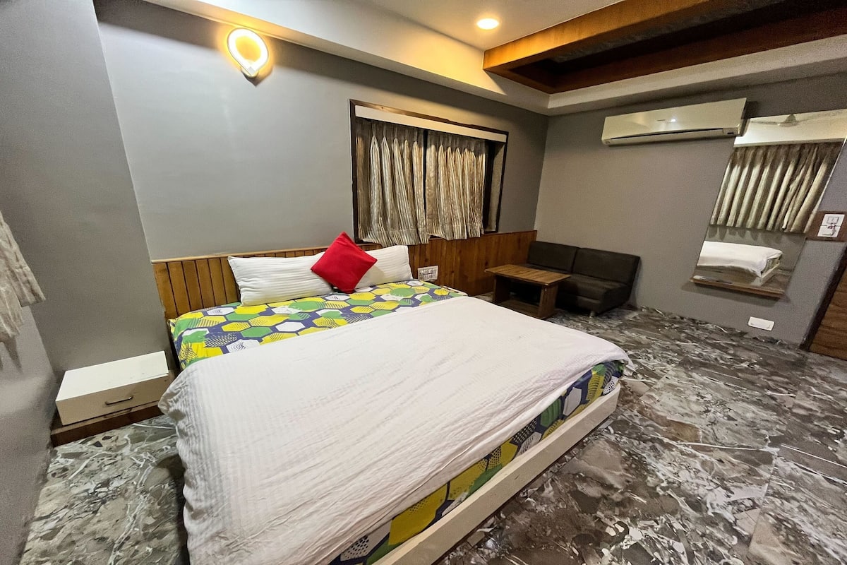 A hotel room with a bed, a desk, and an air conditioning unit.