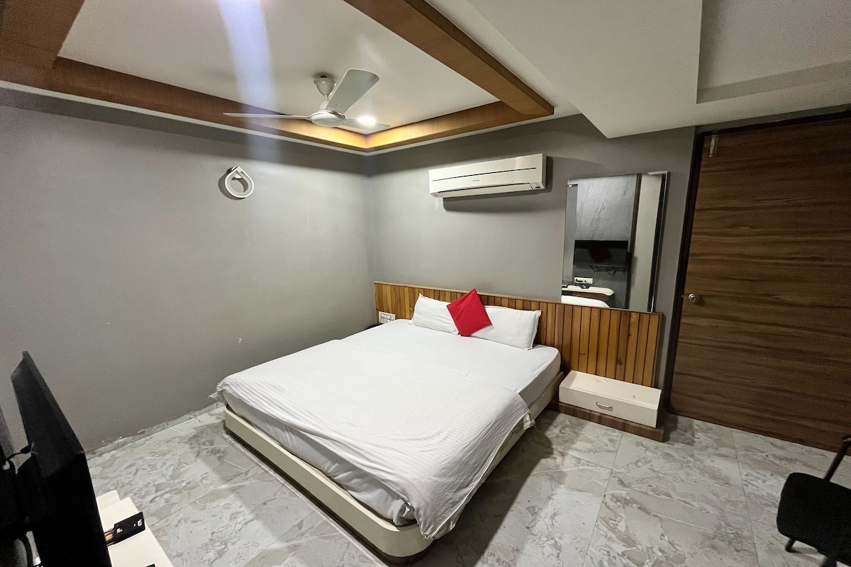 A bedroom with a bed, an air conditioner, a ceiling fan, a wooden headboard, a nightstand, a mirror, and a wardrobe.