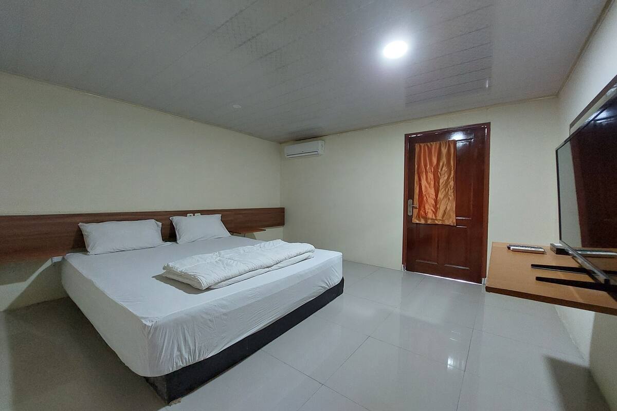Una habitación de hotel con una cama grande, un cabecero de madera, un televisor de pantalla plana y una puerta de madera con cortina.