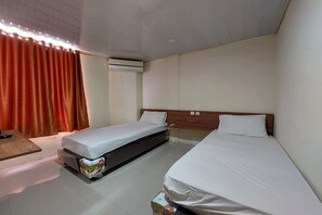 Une chambre d’hôtel avec deux lits simples, une tête de lit en bois, un appareil de climatisation et une petite table.
