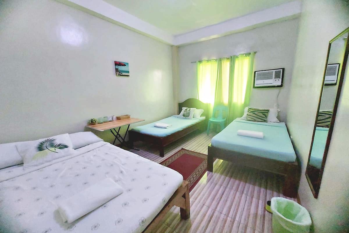A hotel room with two single beds, a small table, a chair, a waste bin, and a window with curtains.