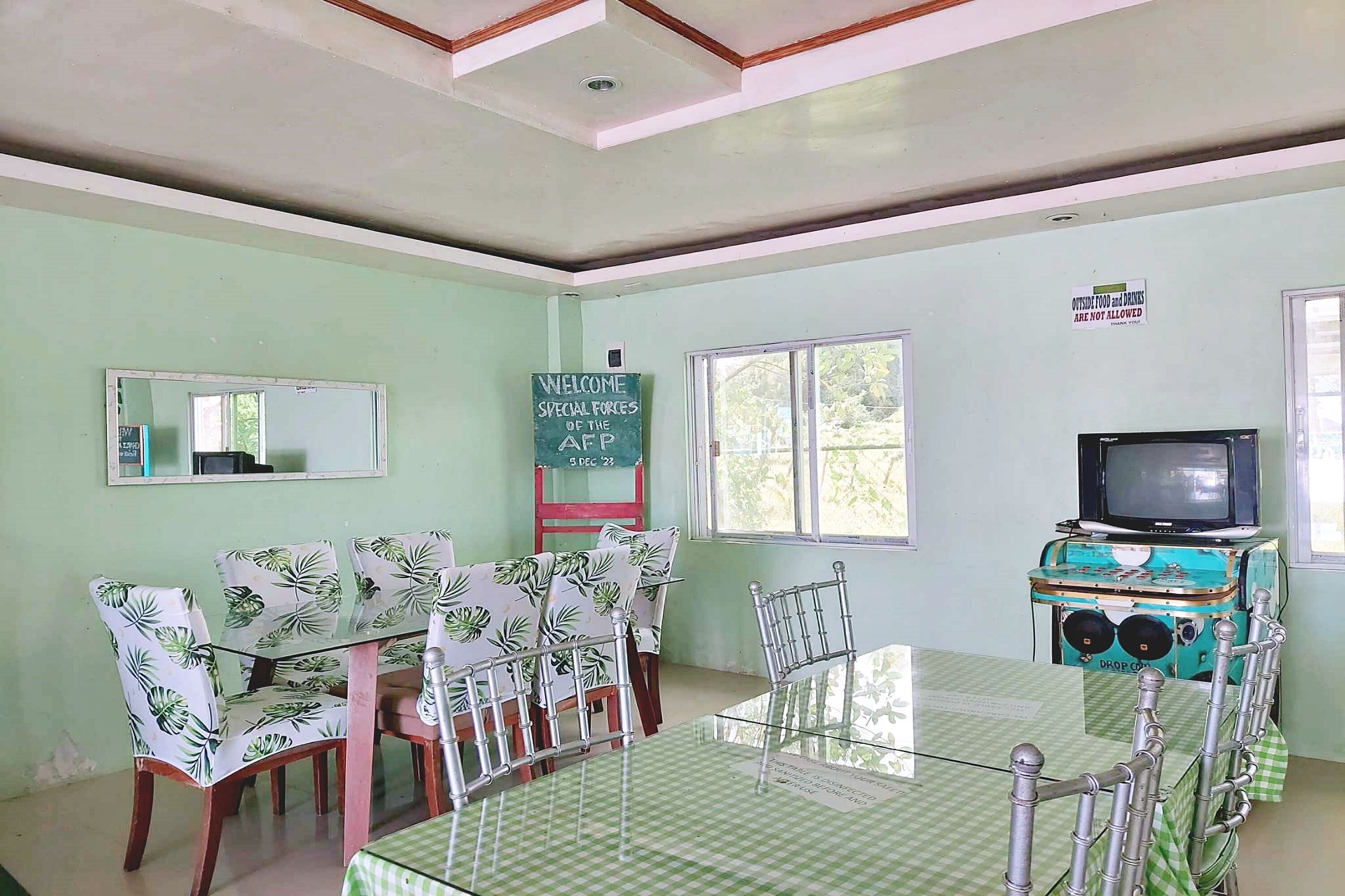 A dining area with a glass table and chairs, a television on a vintage cabinet, and a welcome sign for the AEP Special Forces.
