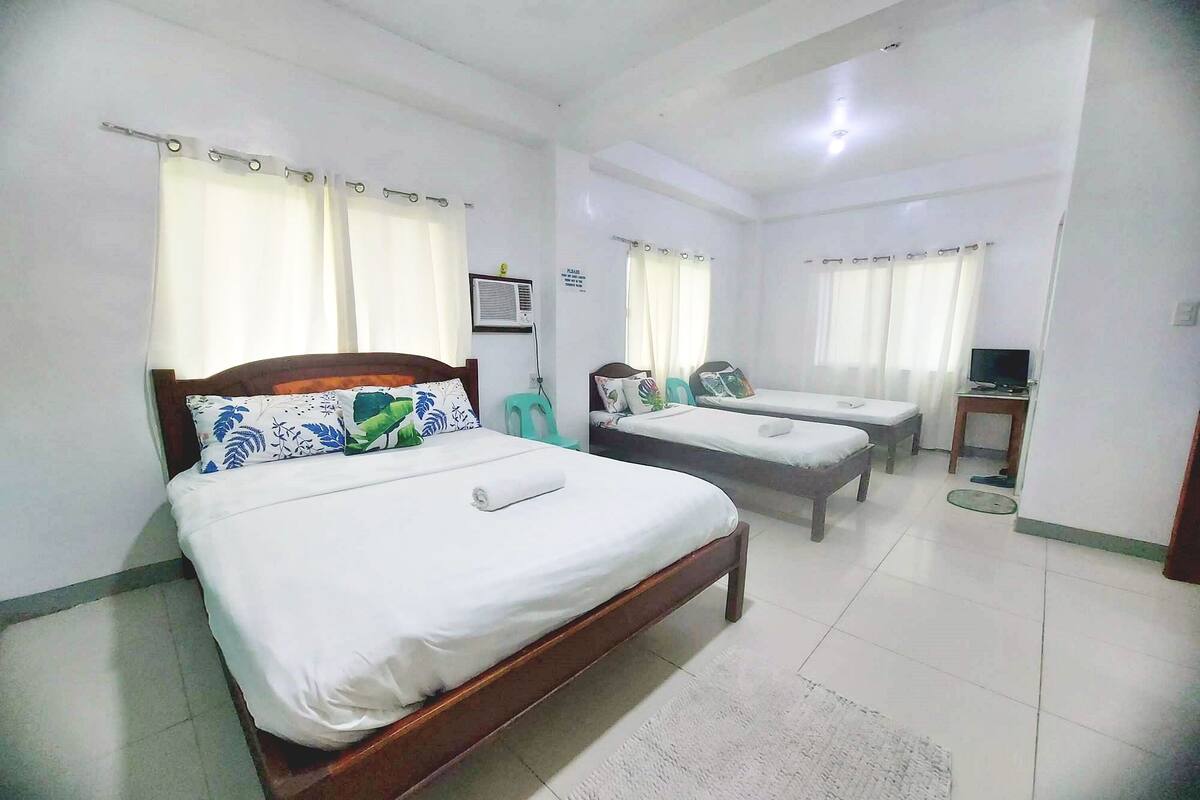 A hotel room with a large bed, a smaller bed, a desk, and a television.