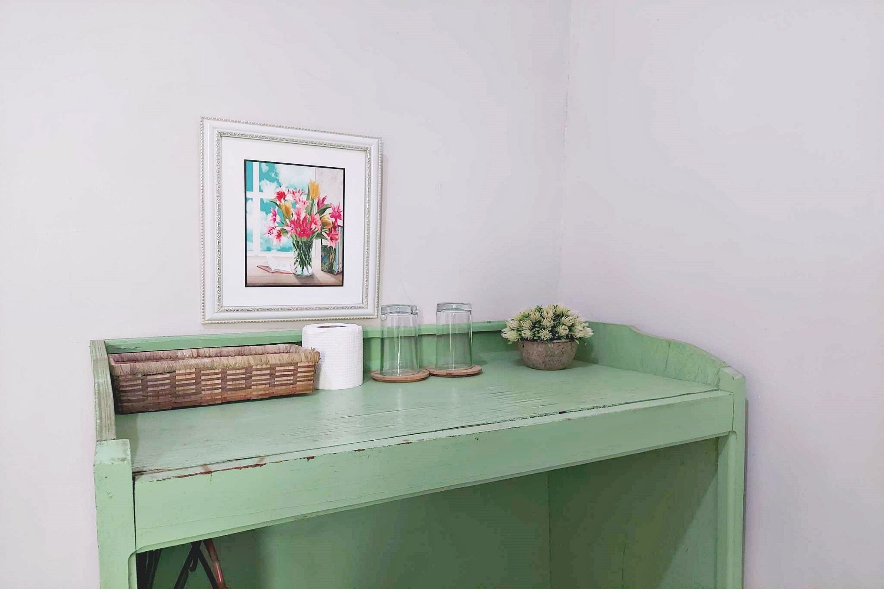 Een groen geschilderde bank met een lijstfoto van bloemen, een mand en een kleine potplant.