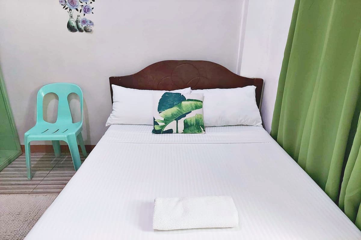 A neatly made bed with white bedding and a green pillow, a green chair, and a green curtain.