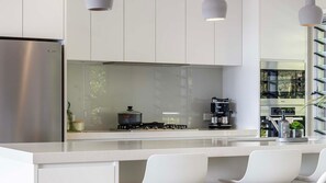 A modern kitchen with a stainless steel refrigerator, a gas stove, a coffee maker, and a large window.