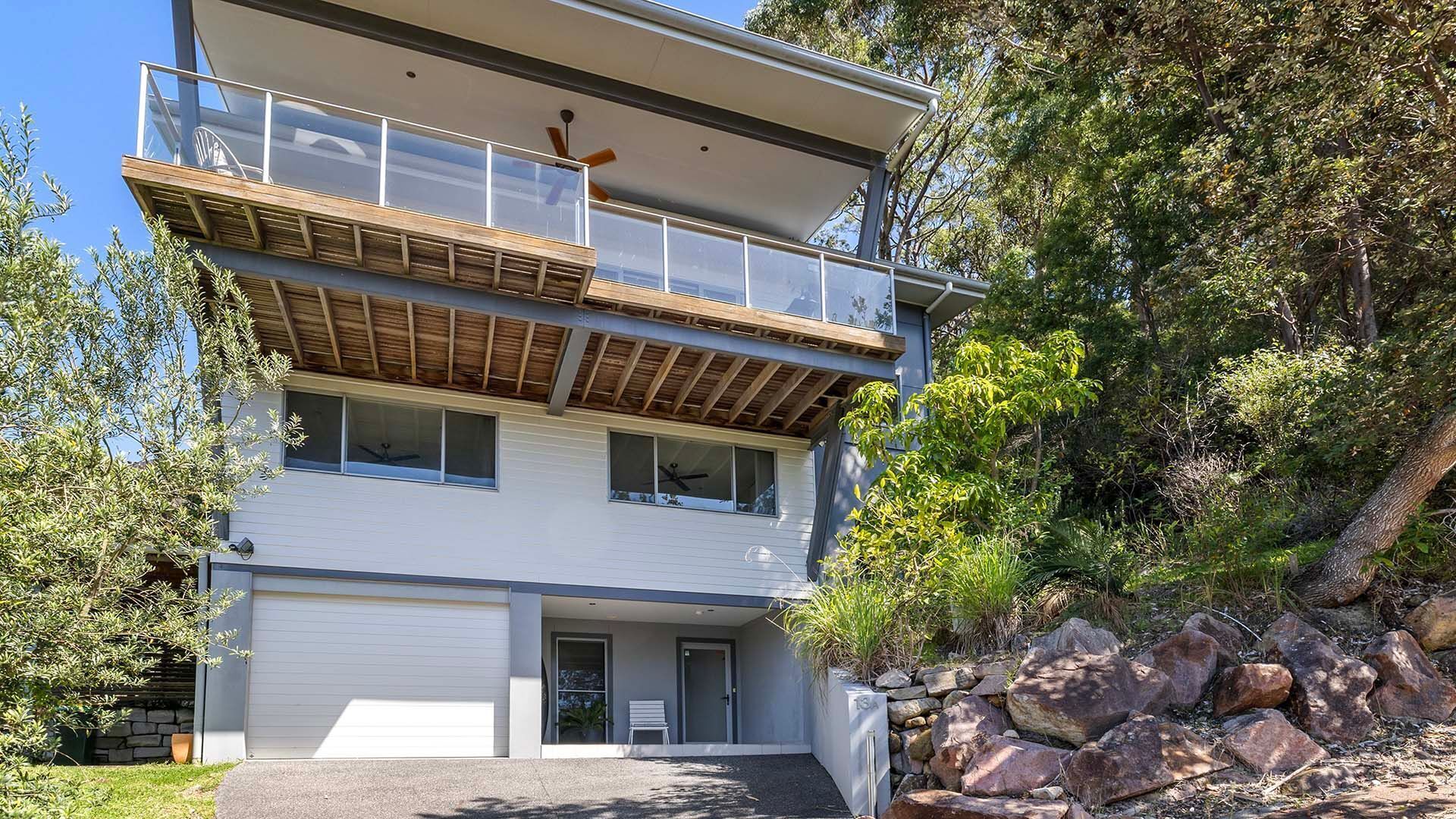 Ein modernes, zweistöckiges Haus mit Balkon, Garage und einer Mauer aus Naturstein.