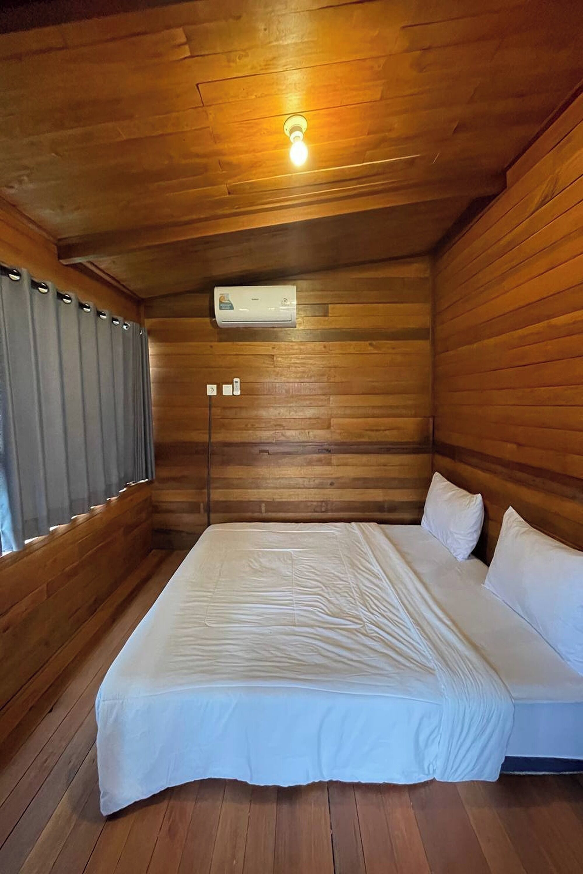 Una habitación tipo cabaña de madera con una cama, una ventana con cortinas y una lámpara en el techo.