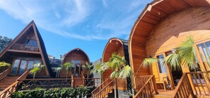 A row of wooden cabins with balconies, each featuring a staircase and surrounded by potted plants. - Umah Nanda (Kintamani)